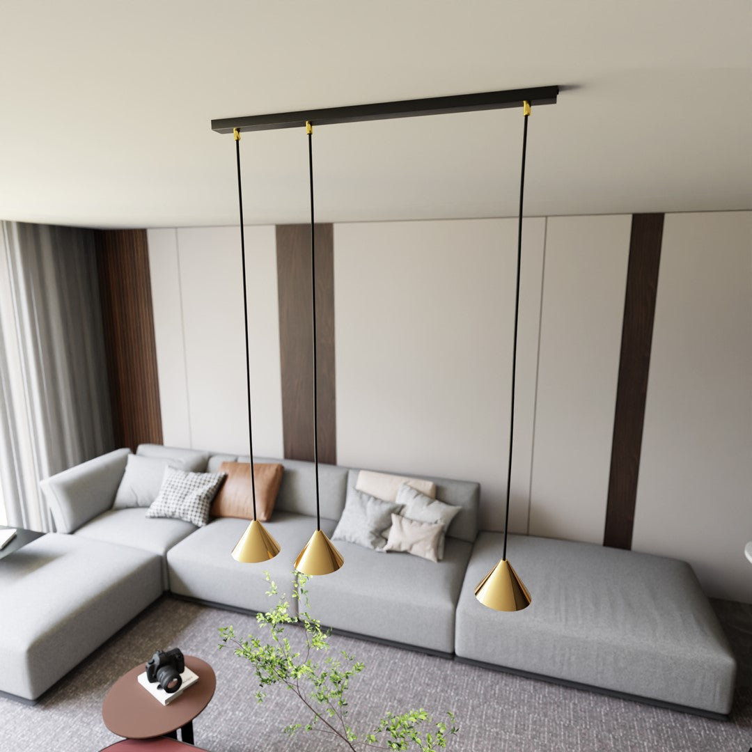 Ambiance salon : les trois cônes dorés pendent au-dessus d'un canapé d'angle gris, lumière chaude.