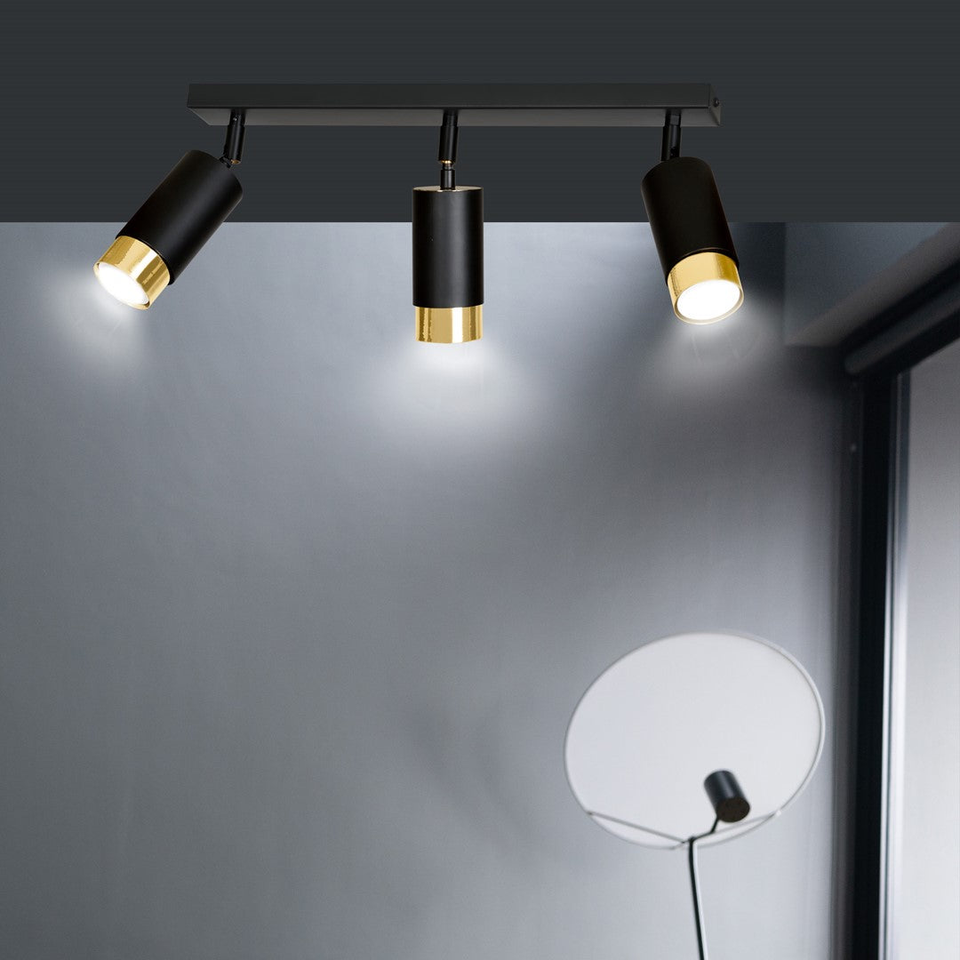 Plafonnier fixé au plafond au-dessus d'un mur gris, éclairage orientable des trois têtes.