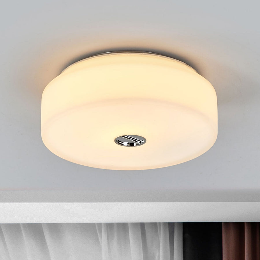 Plafonnier rond allumé, fixé au plafond, diffuseur en verre blanc et bouton central chromé.