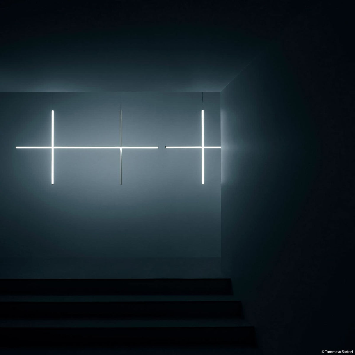Mise en ambiance sombre avec trois appliques croix lumineuses fixées au mur.