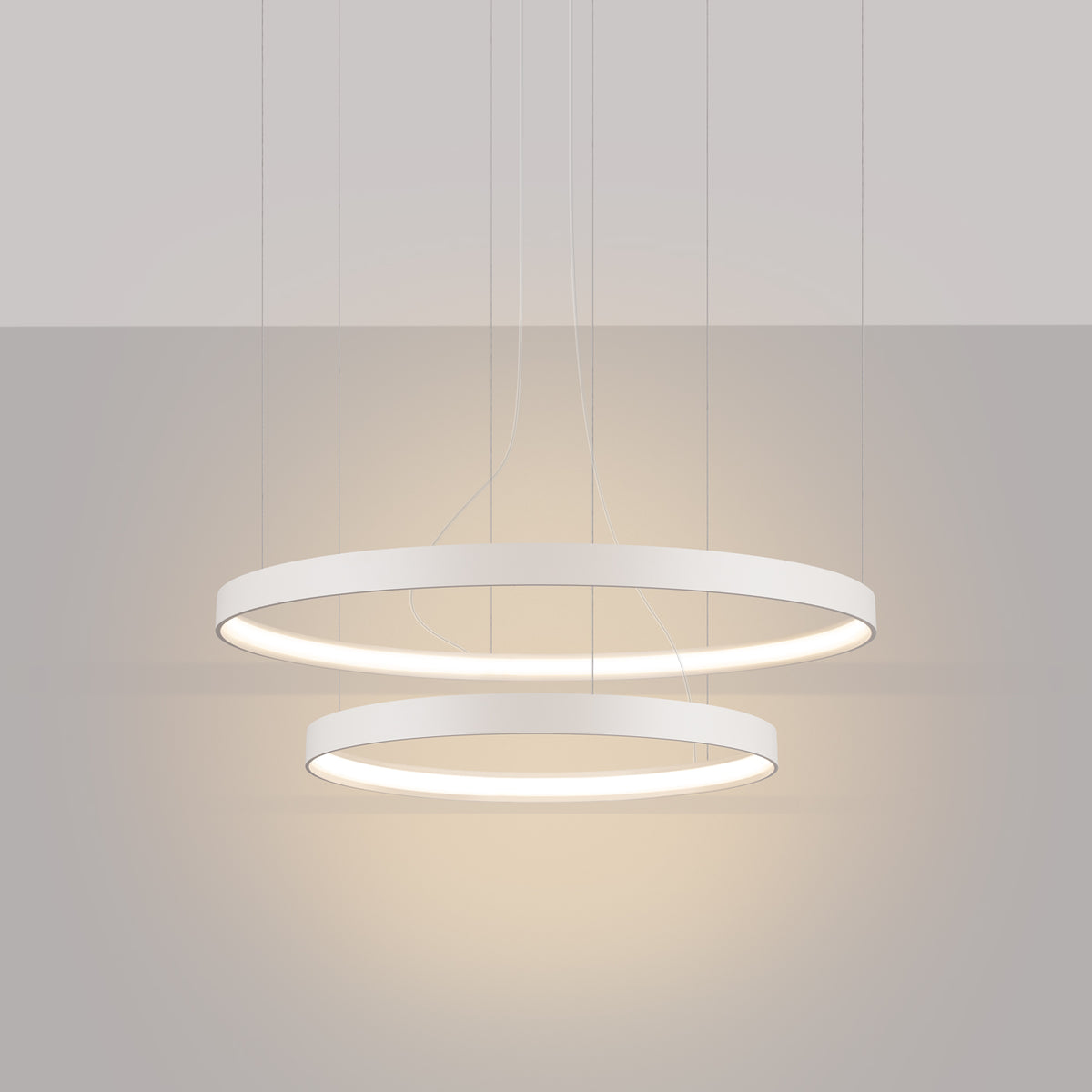 Mise en ambiance du lustre deux anneaux allumé dans une pièce aux murs gris.