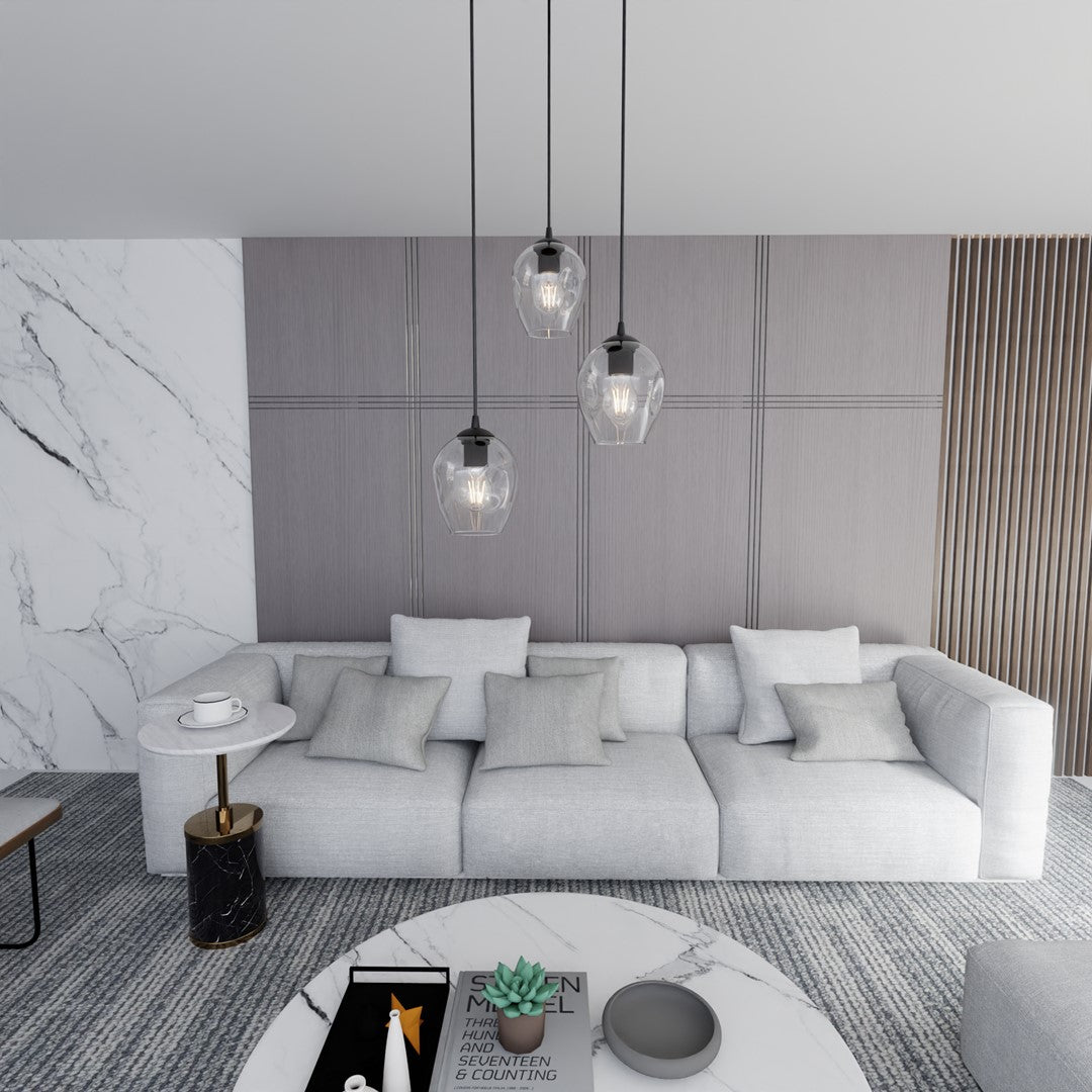 Mise en ambiance salon contemporain avec suspension noire trois lumières allumées et canapé gris.