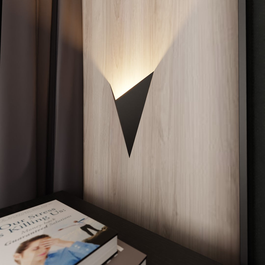 Applique murale triangulaire noire éclairant un mur en bois clair derrière un lit.