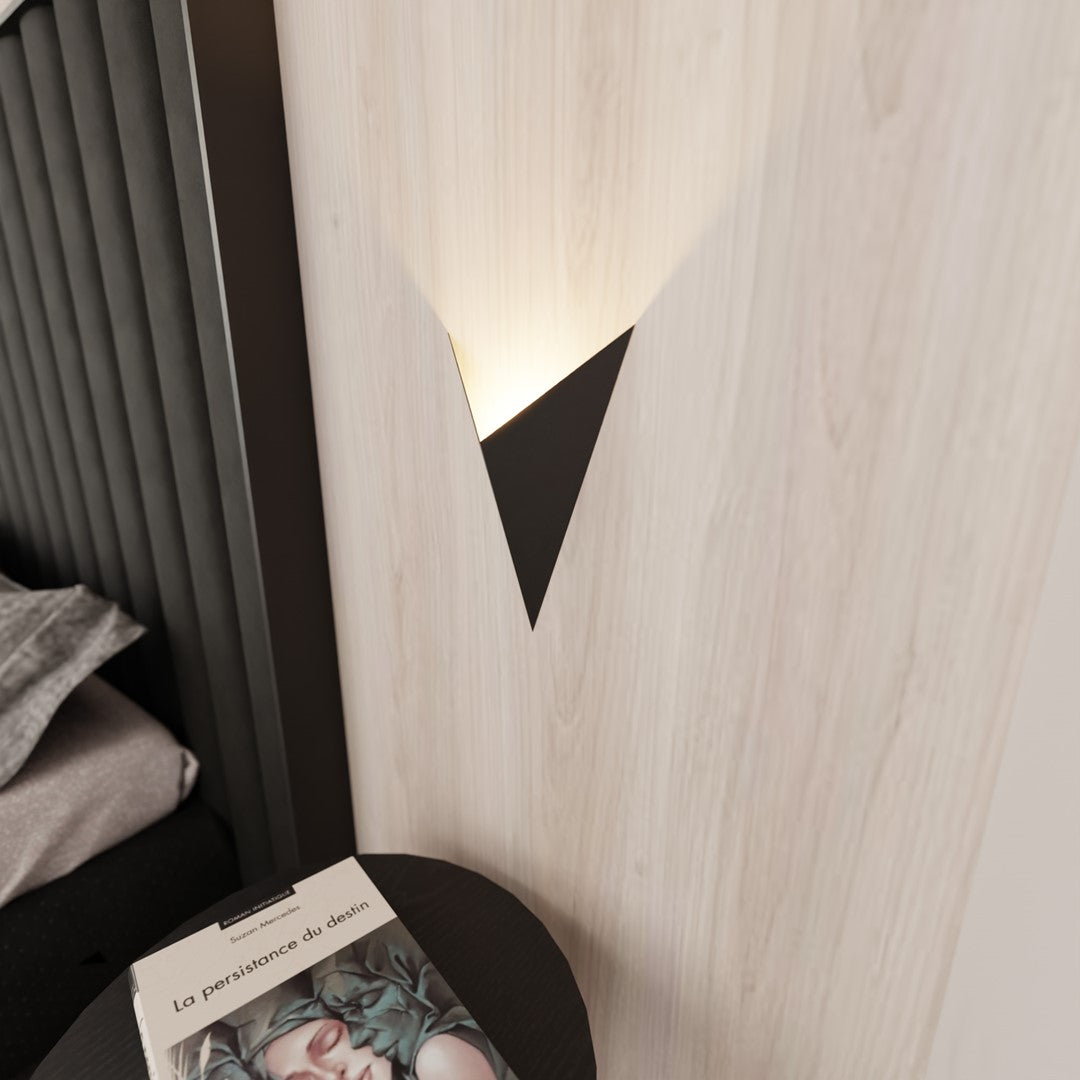 Détail de l'applique murale noire projetant une lumière chaude sur le mur.