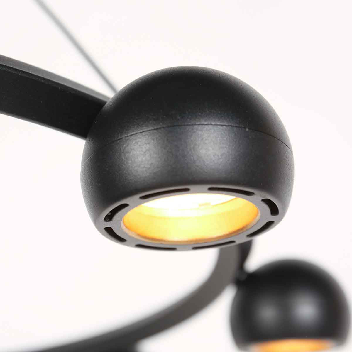 Détail d'un luminaire sphérique noir, diffuseur en verre et lumière chaude.