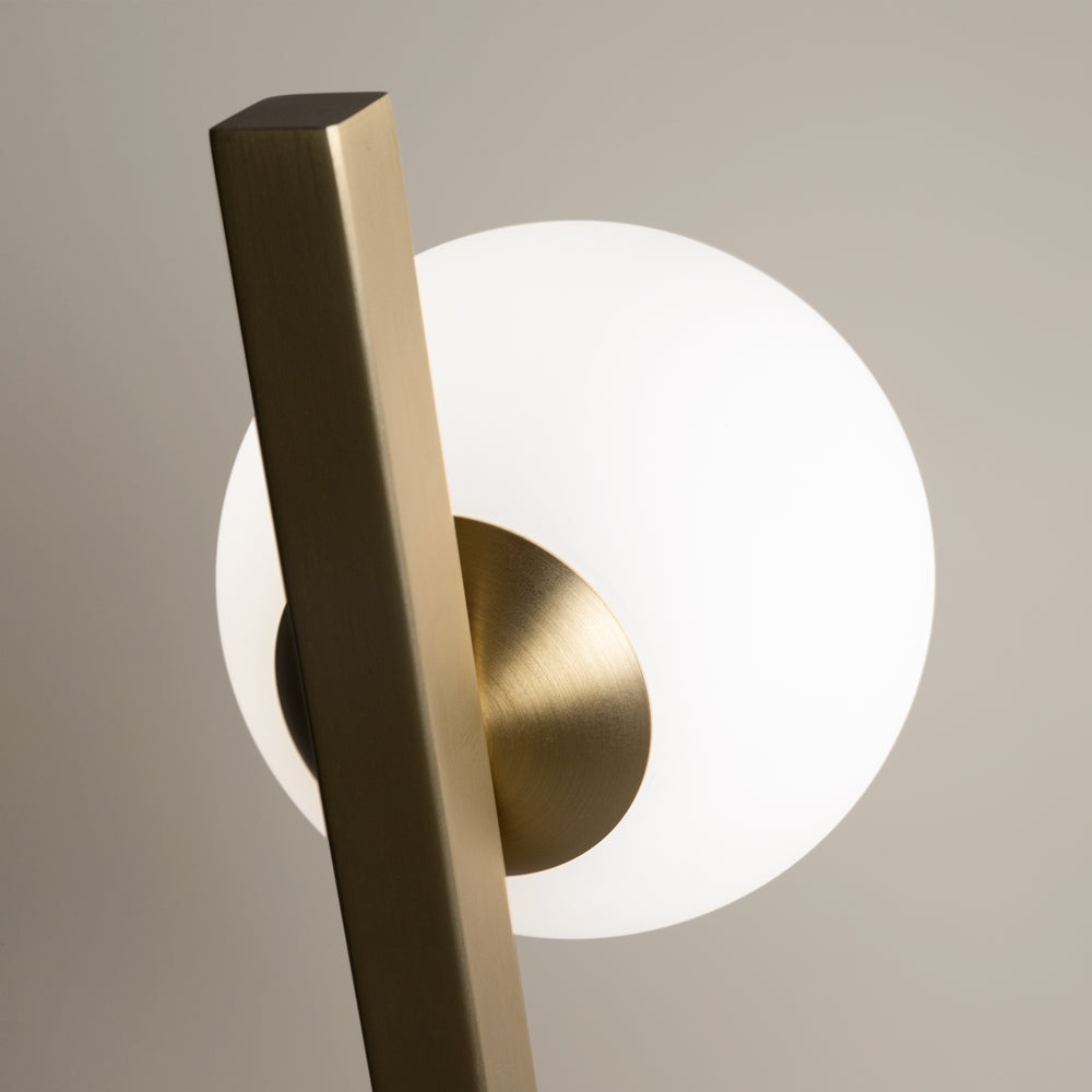 Détail rapproché de la sphère en verre blanc et du support doré brossé.