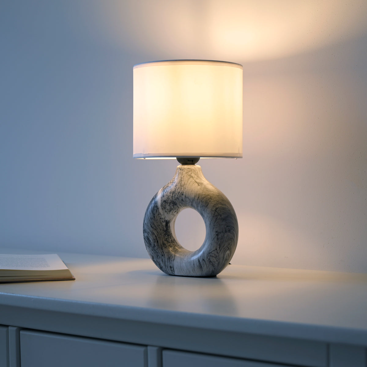 Mise en ambiance sur meuble blanc, lampe allumée près d'un livre ouvert