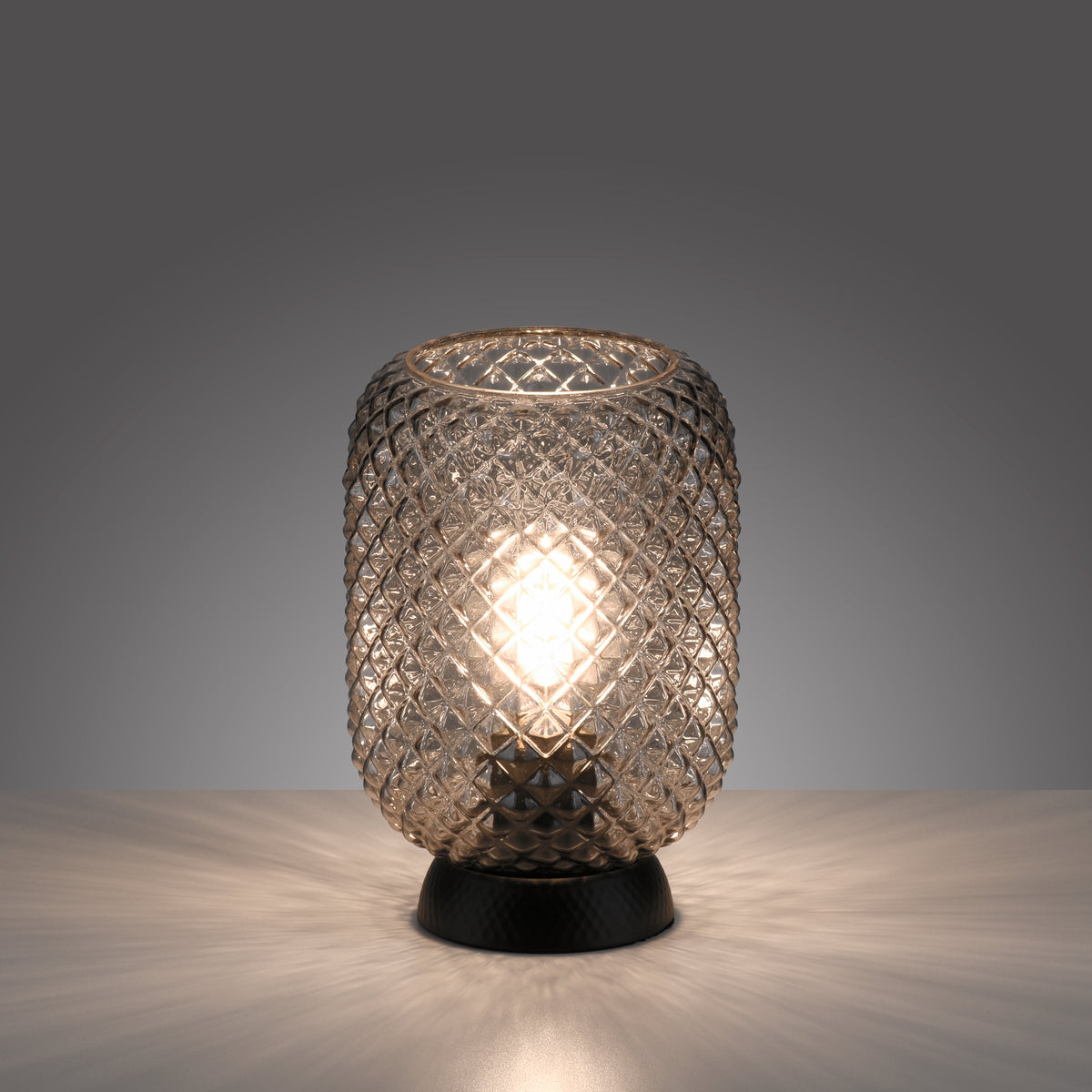 Lampe à poser allumée sur surface claire, halo lumineux projeté sur fond gris.