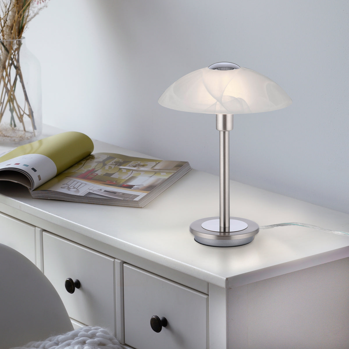 Mise en ambiance de la lampe allumée sur une commode blanche avec magazine