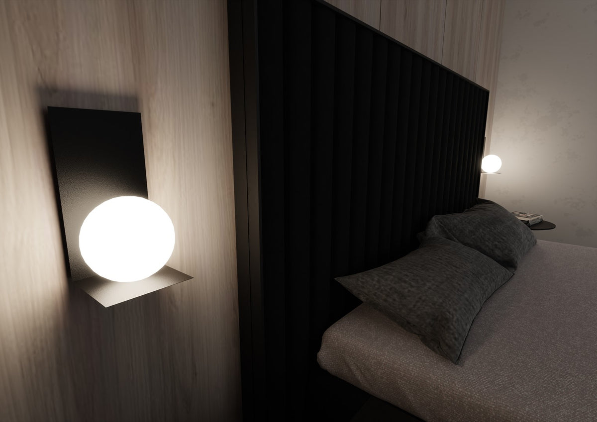 Vue nocturne d'une applique allumée éclairant un lit aux coussins gris foncé.