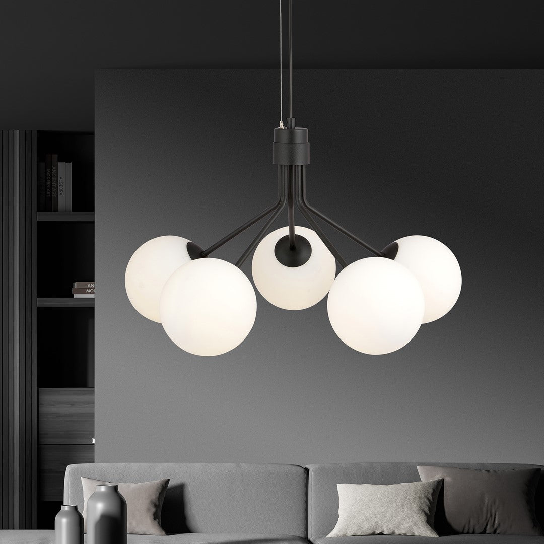 Luminaire suspendu noir allumé dans un intérieur sombre, au-dessus d'un canapé gris.