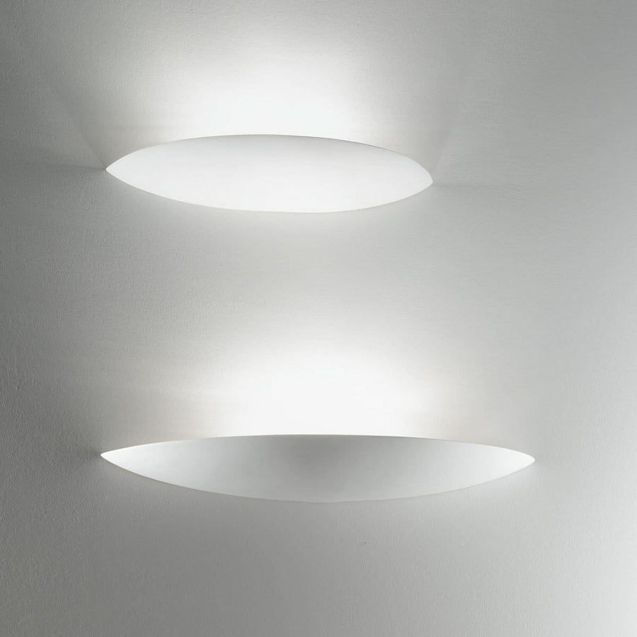 Deux appliques ovales allumées superposées sur un mur clair, halo lumineux diffus