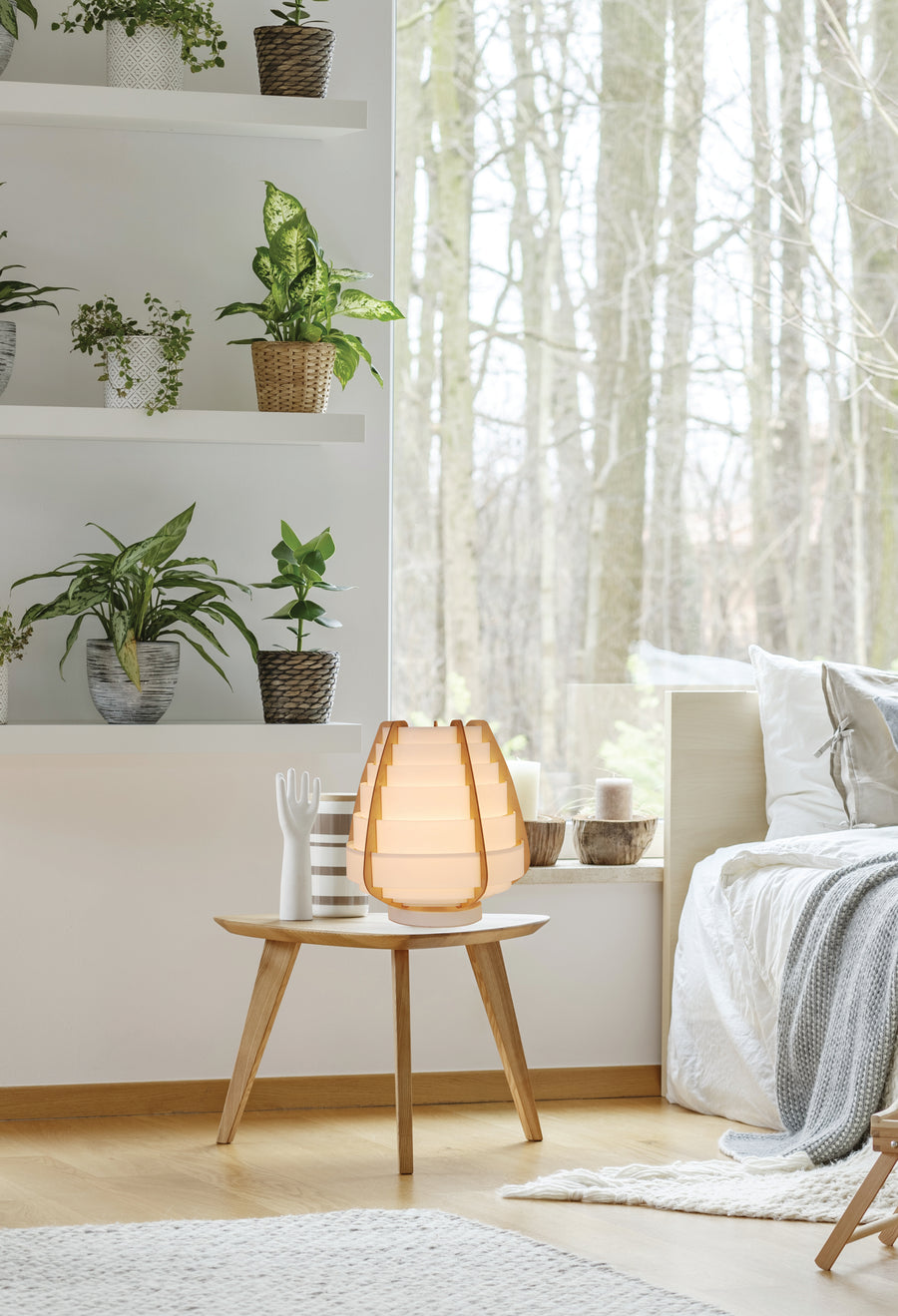 Lampe posée sur une table basse dans une chambre claire avec plantes vertes.
