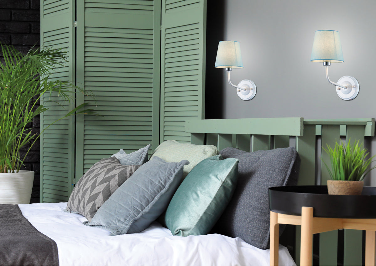 Mise en ambiance chambre, deux appliques murales allumées au-dessus du lit à coussins.