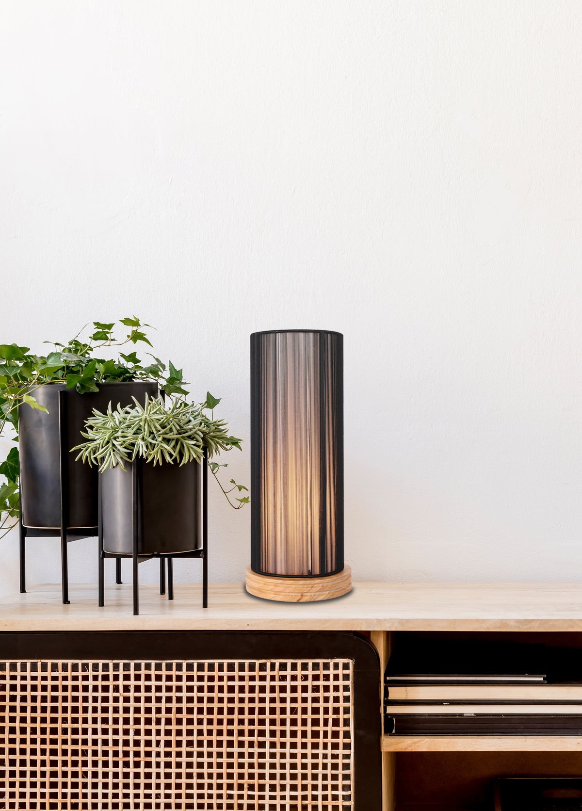 Mise en ambiance sur buffet cannagé, lampe posée près de plantes vertes en potées noires