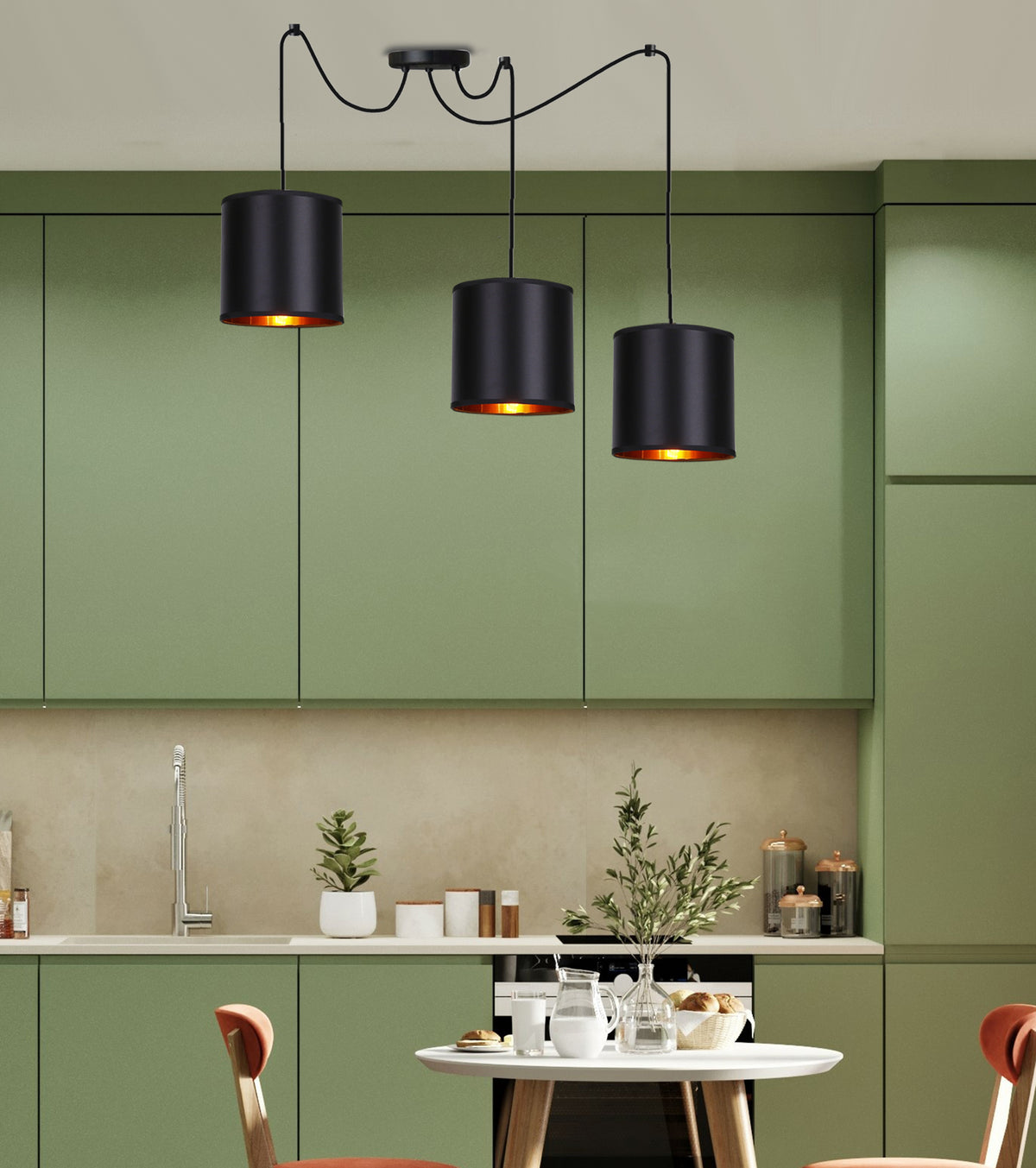 Mise en ambiance dans une cuisine verte, trois suspensions noires au-dessus d'une table dressée.