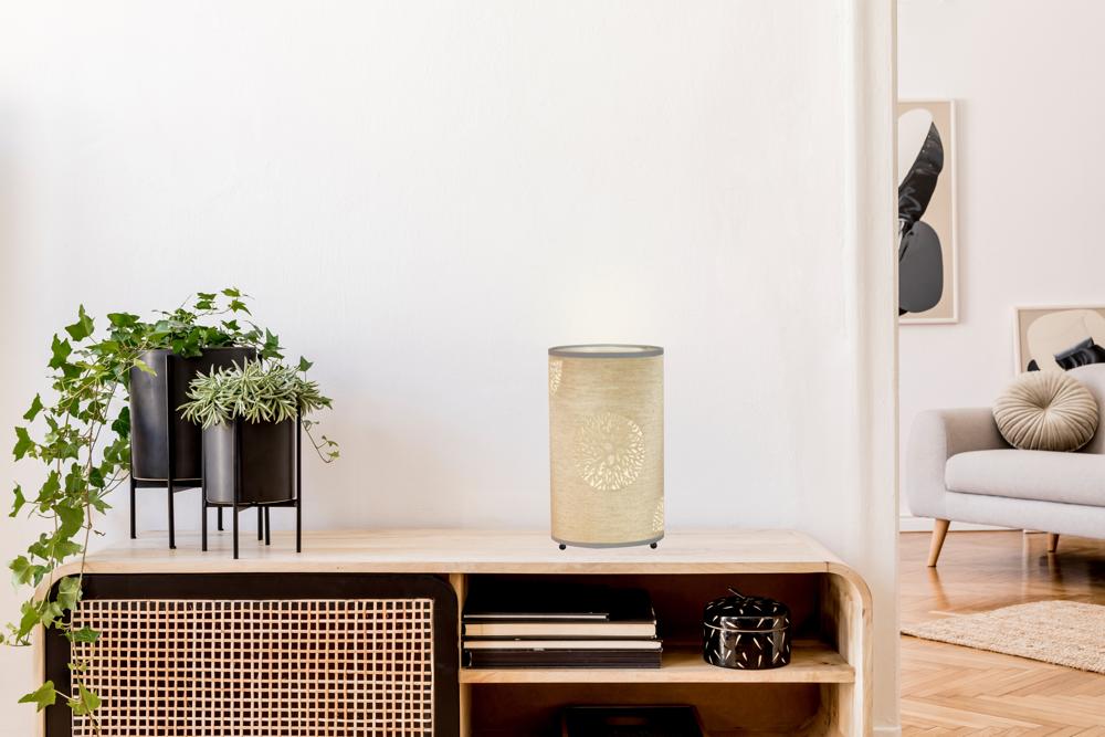 Lampe beige éteinte sur le meuble, entourée de plantes vertes et d'objets noirs.