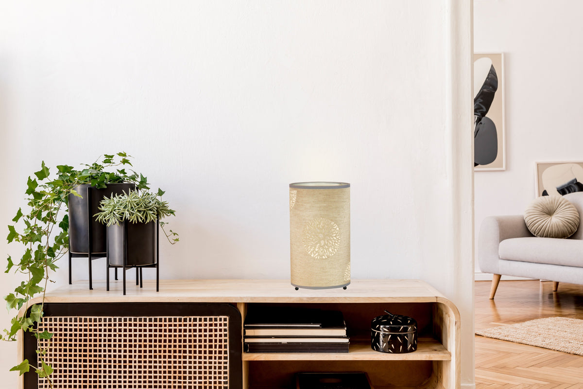 Lampe beige allumée posée sur un meuble en bois dans un salon clair.