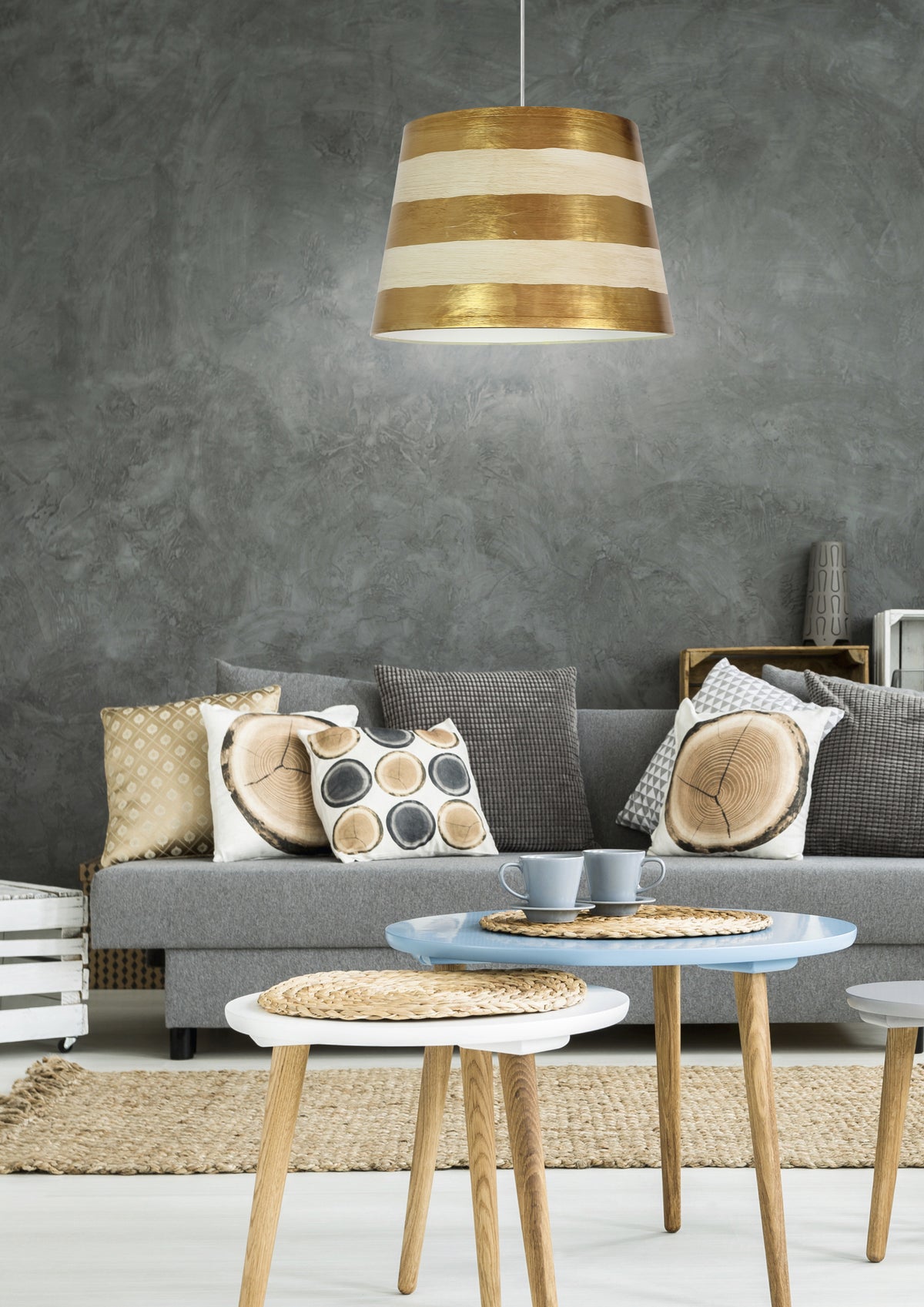 Suspension au-dessus d'un canapé gris, coussins à motifs et tables basses en bois clair.