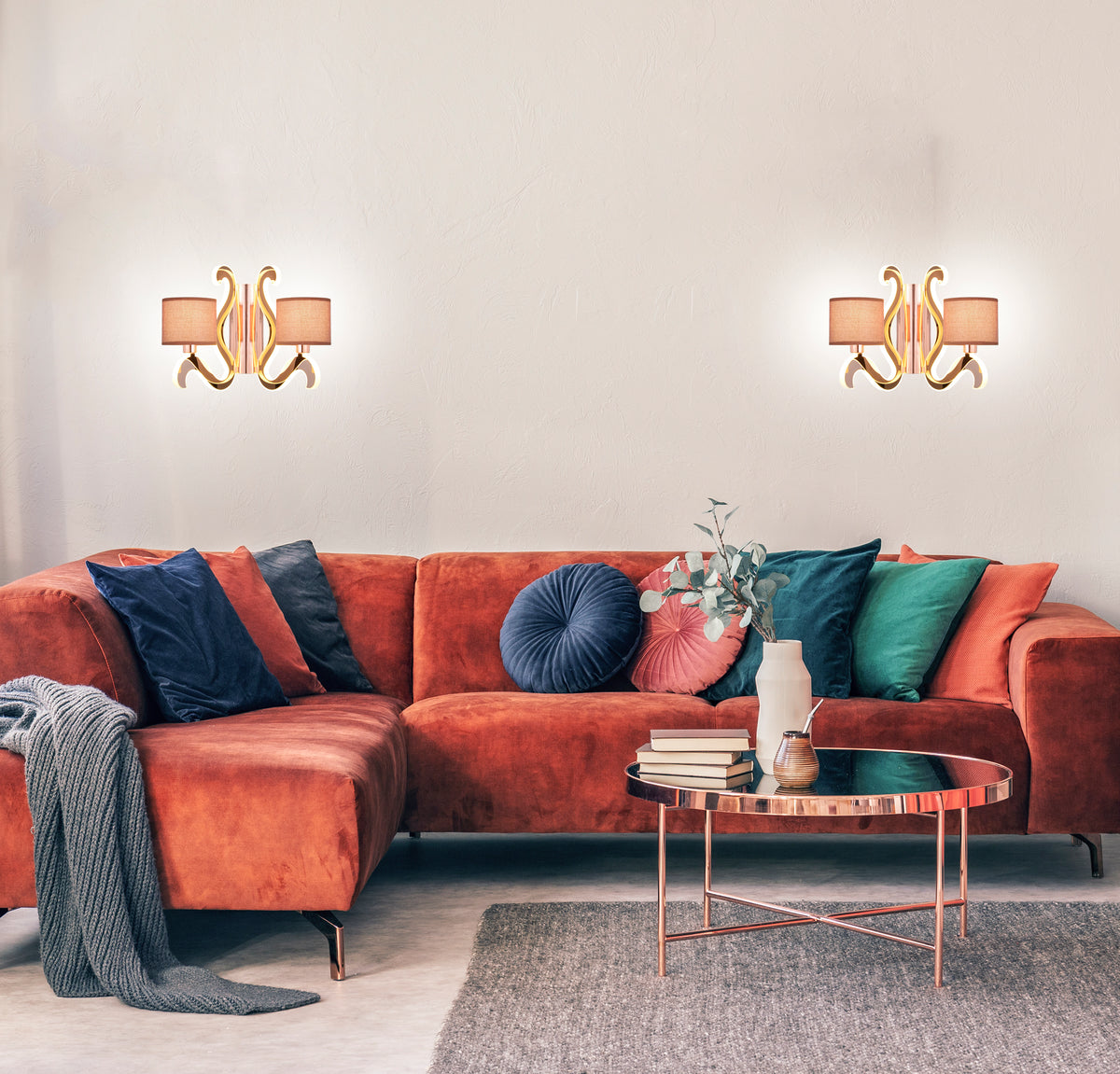 Deux appliques murales identiques éclairent un séjour avec canapé orange et coussins multicolores.
