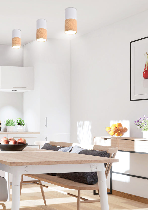 Trois luminaires cylindriques blanc et bois installés au plafond dans une salle à manger moderne.