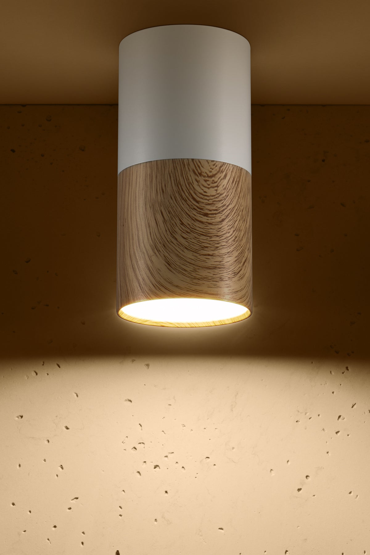 Luminaire cylindrique blanc et bois allumé, fixé au plafond, éclairant un mur en béton.