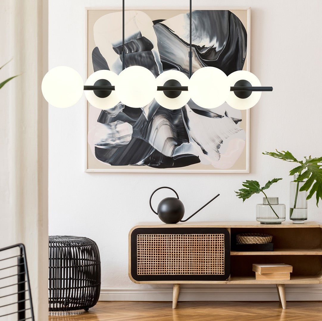 Mise en ambiance au-dessus d'un meuble, suspension allumée devant un tableau abstrait.