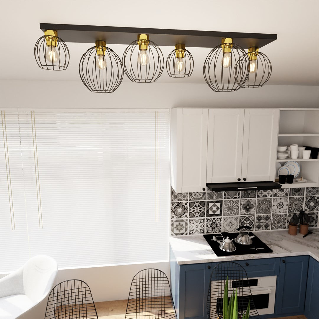 Luminaire allumé dans une cuisine, six globes grillagés suspendus devant meubles blancs et crédence mosaïque.