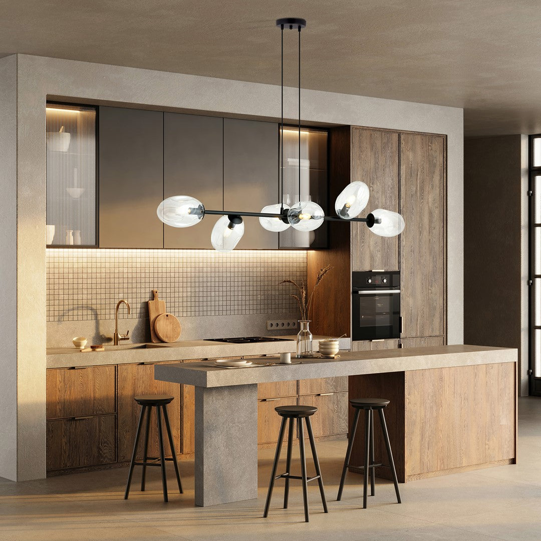 Luminaire suspendu au-dessus d'un îlot de cuisine en bois clair avec tabourets noirs