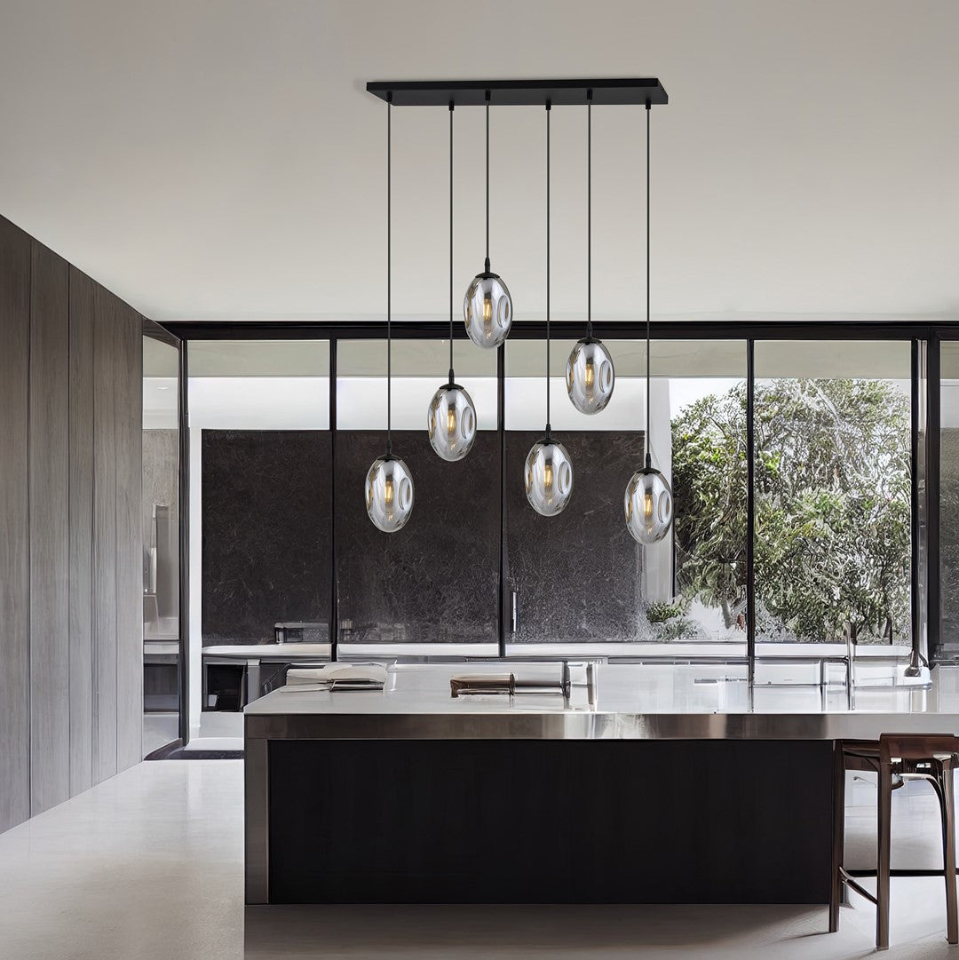 Suspension installée au-dessus d'un îlot de cuisine, grandes baies et jardin en fond