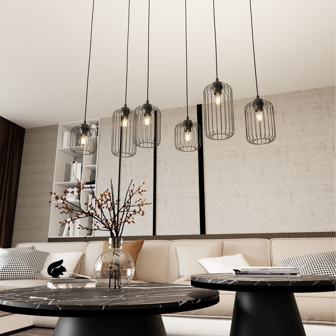 Luminaire suspendu allumé dans un salon, tables basses noires et décoration végétale.