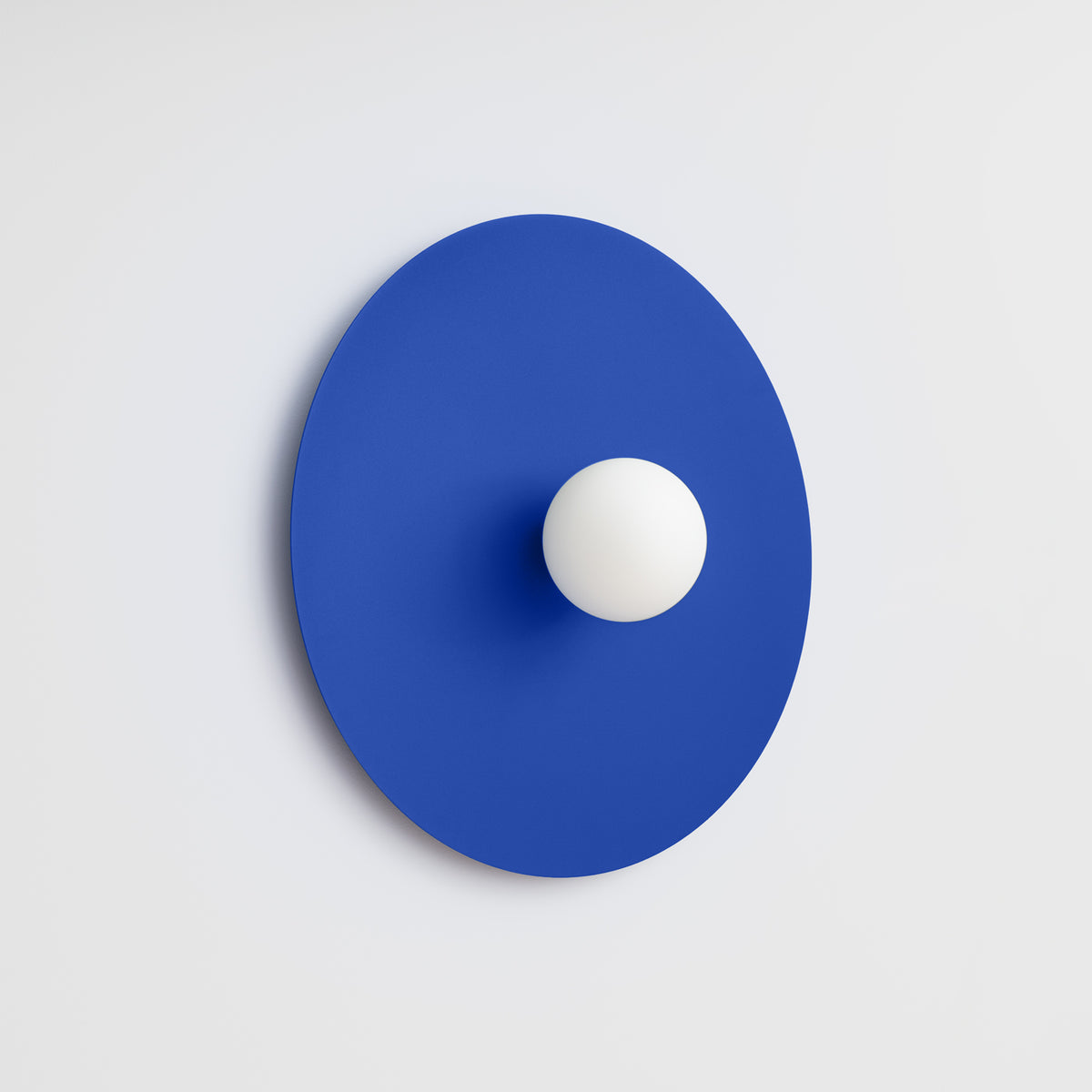 Applique bleue fixée sur un mur blanc clair, légère ombre portée