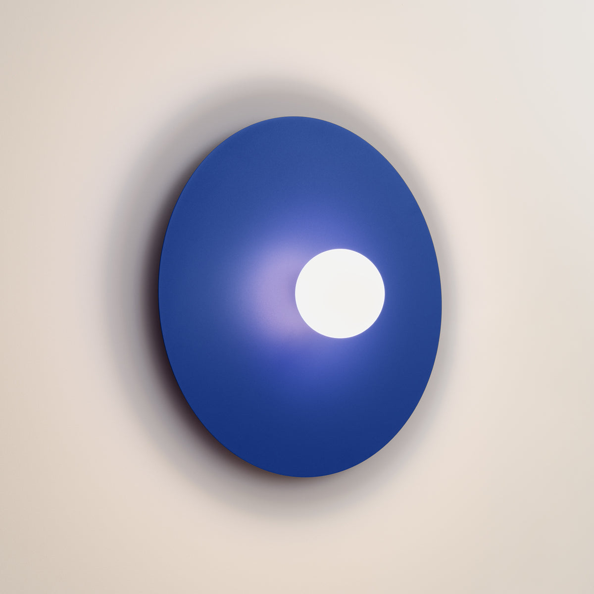 Luminaire allumé sur mur beige, halo blanc diffus autour de la sphère