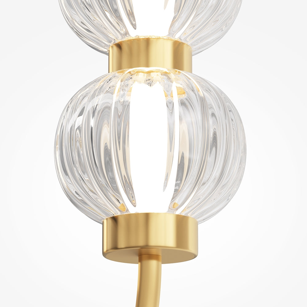 Détail rapproché d'une sphère de verre transparent strié entre deux colliers dorés.