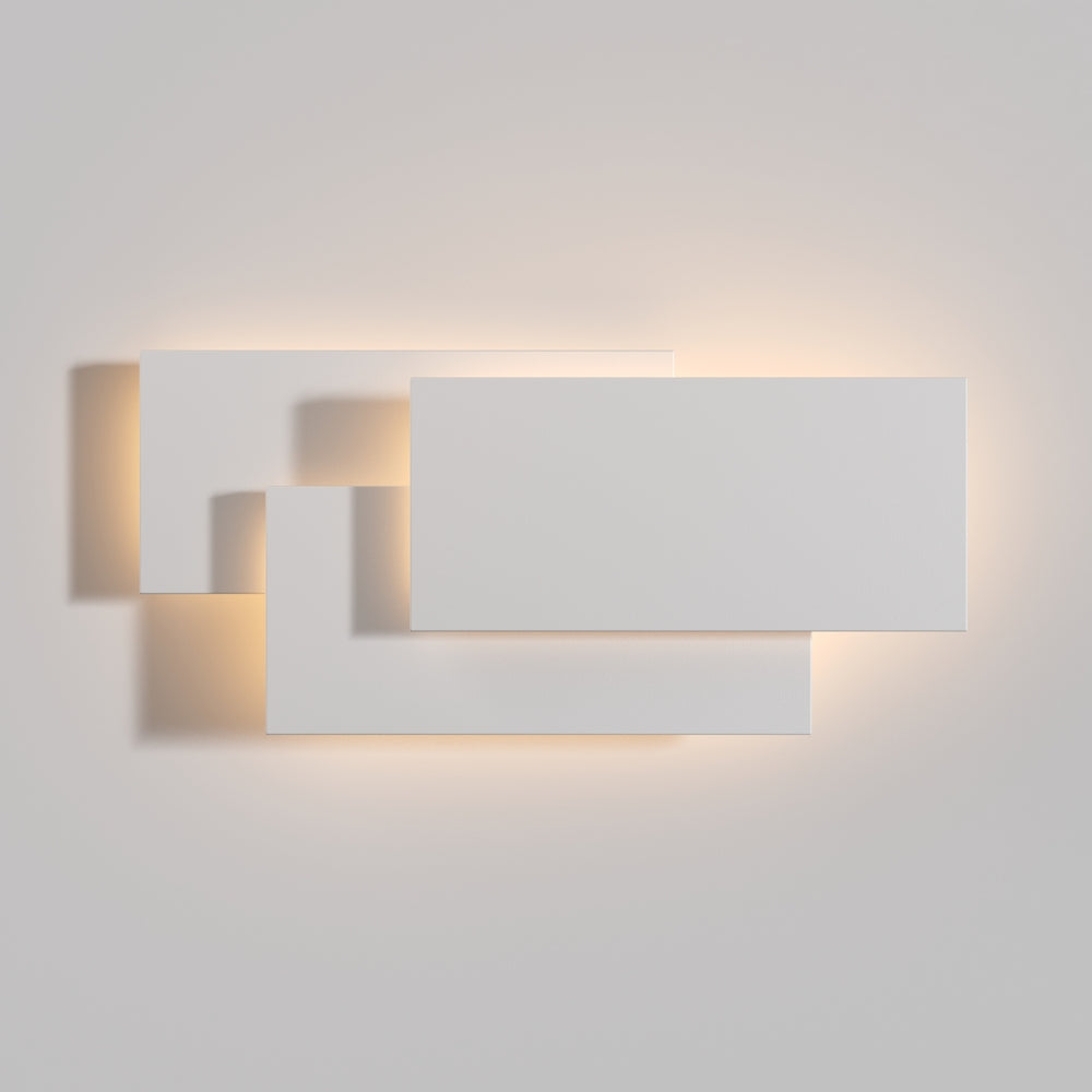 Applique allumée sur mur clair, ombres douces projetées par les panneaux décalés