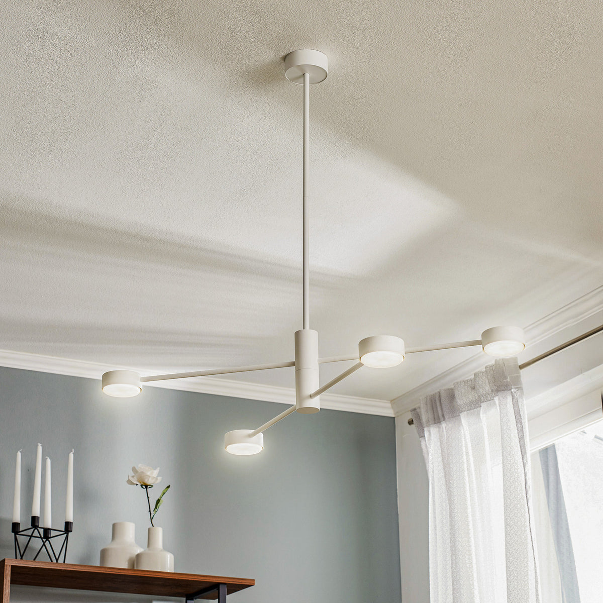 Suspension blanche à quatre bras visible au-dessus d’un meuble avec bougies
