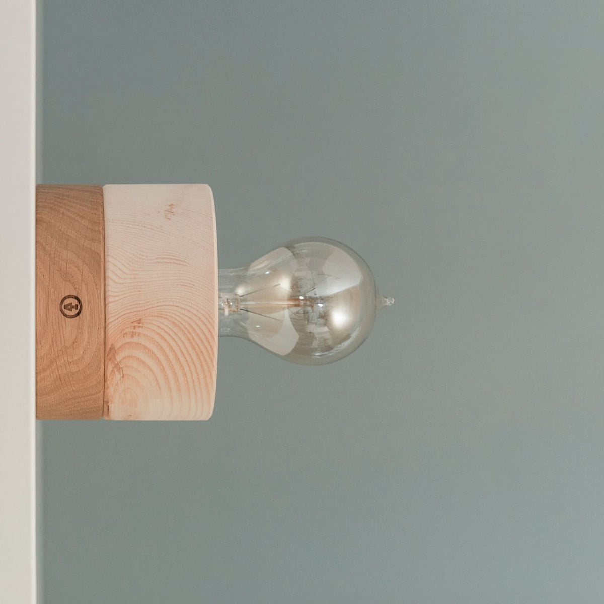 Mise en ambiance de l’applique fixée au mur, bois clair et ampoule visible.