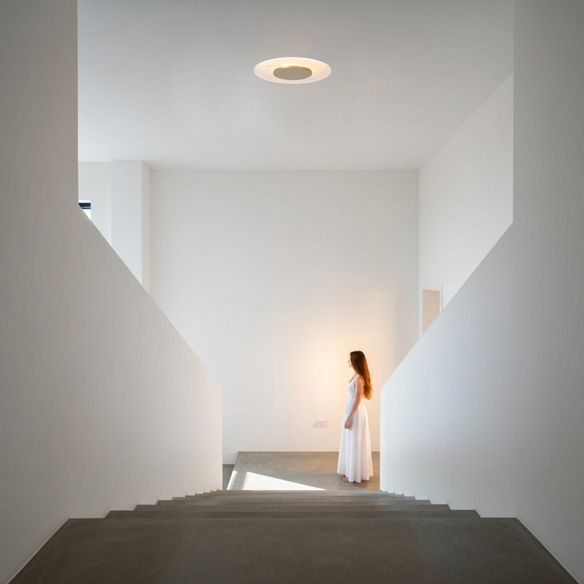 Mise en ambiance dans une cage d'escalier blanche, plafonnier allumé au plafond.