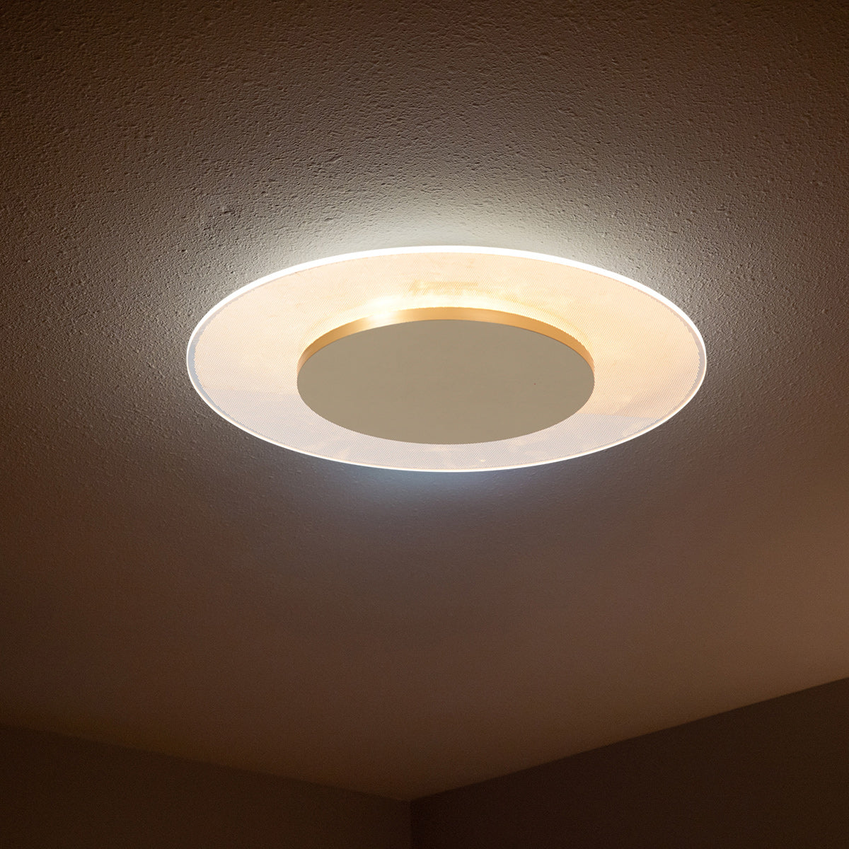 Plafonnier installé au plafond, allumé, halo chaud sur surface texturée.