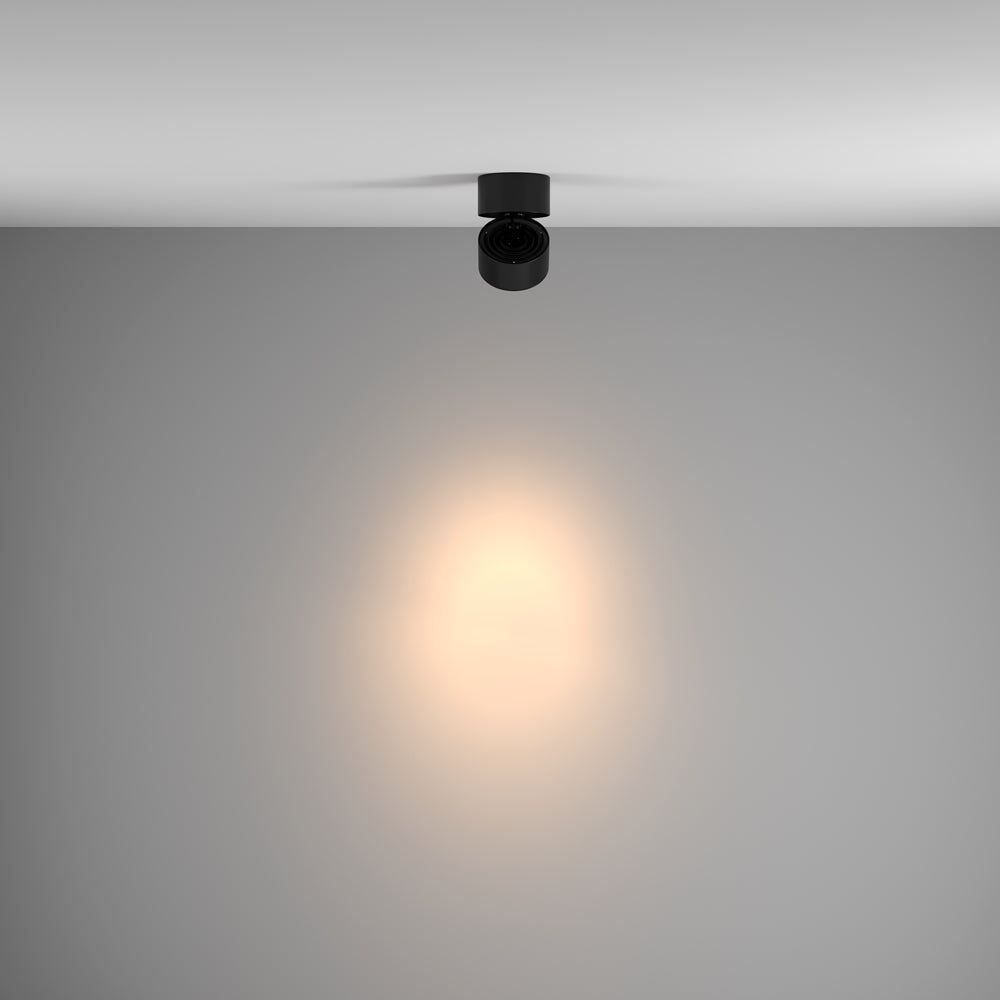 Mise en ambiance d'un plafonnier noir éclairant un mur gris de sa lumière chaude.