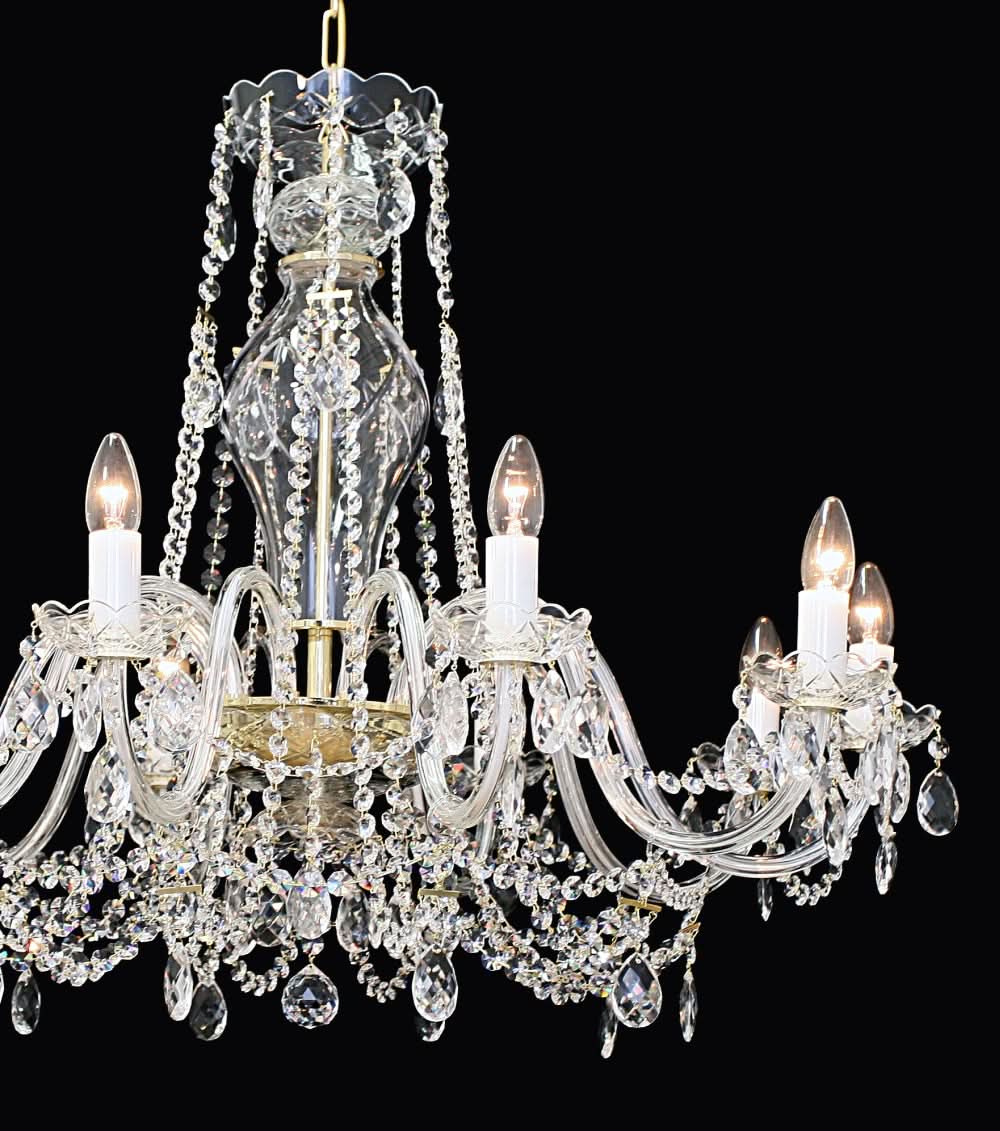 Gros plan du lustre montrant les bras, bobèches et grappes de cristal scintillantes.