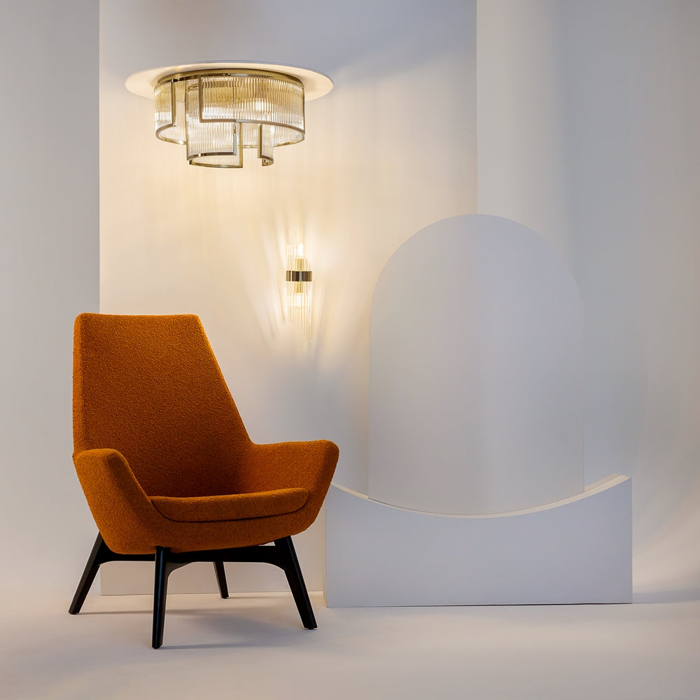 Mise en ambiance avec fauteuil orange, applique murale et plafonnier doré dans pièce blanche