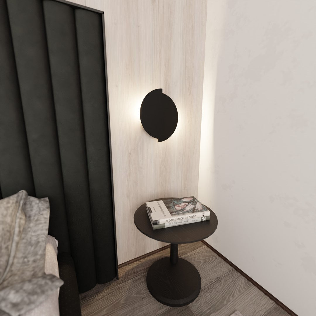 Ambiance de chevet : applique éclairée au-dessus d'une petite table ronde noire