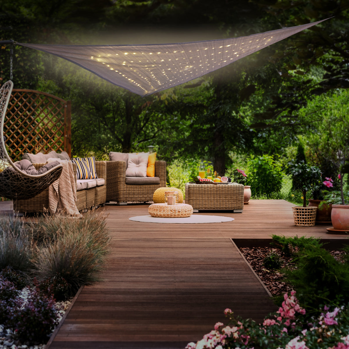 Mise en ambiance extérieure : voile lumineux tendu au-dessus d'un salon de jardin en rotin.