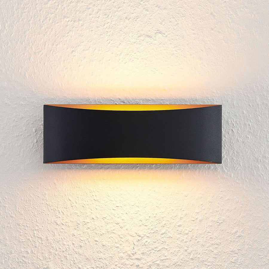 Face avant allumée sur mur crépi, lumière chaude soulignant les bords incurvés noirs.