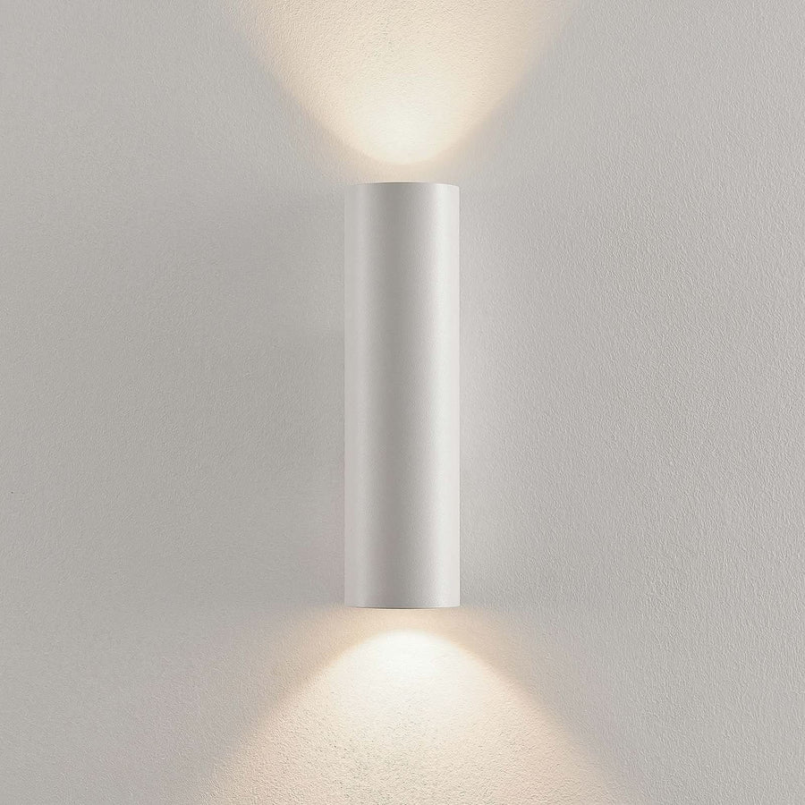 Applique cylindrique blanche installée sur un mur clair, éclairant vers le haut et le bas.