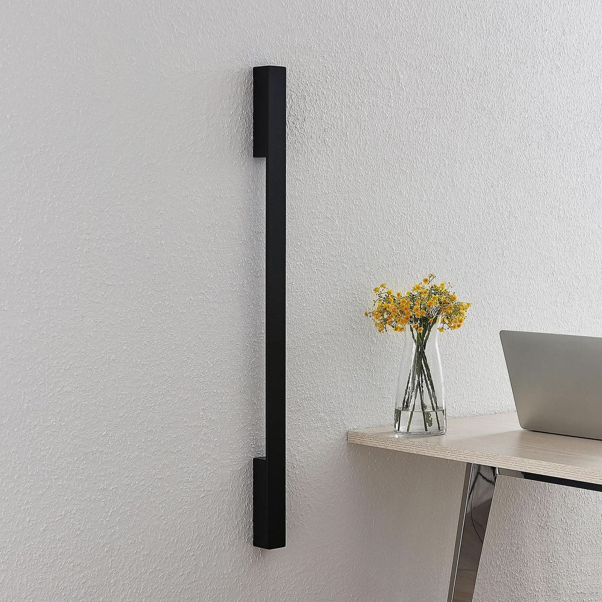 Applique murale noire éteinte fixée au mur, bureau en bois et vase de fleurs jaunes.