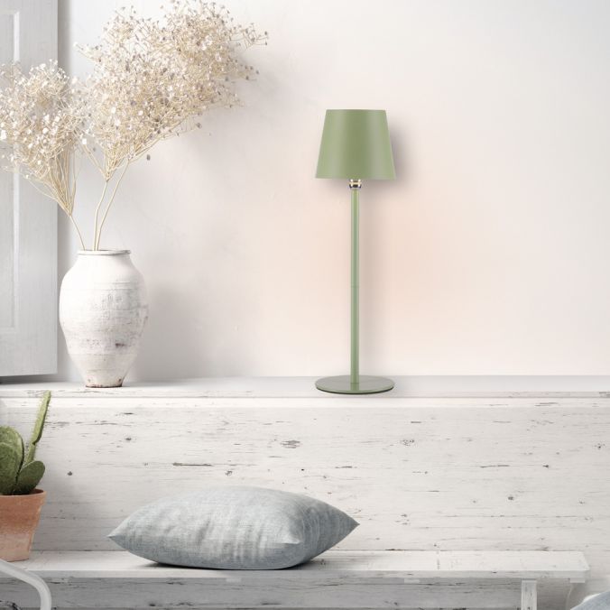 Lampe verte posée sur étagère en bois blanc avec vase de fleurs séchées et coussin gris