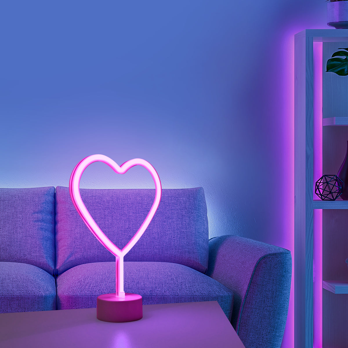 Lampe cœur rose allumée posée sur une table devant un canapé, ambiance violette.