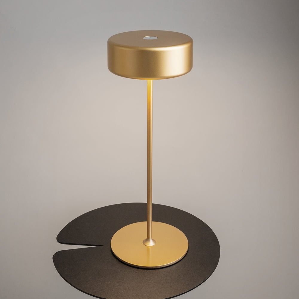 Vue plongeante de la lampe dorée sur plateau noir, base ronde et tige centrale.